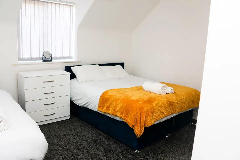 Double bedroom at Humber Hub with a mustard throw and a chest of drawers
