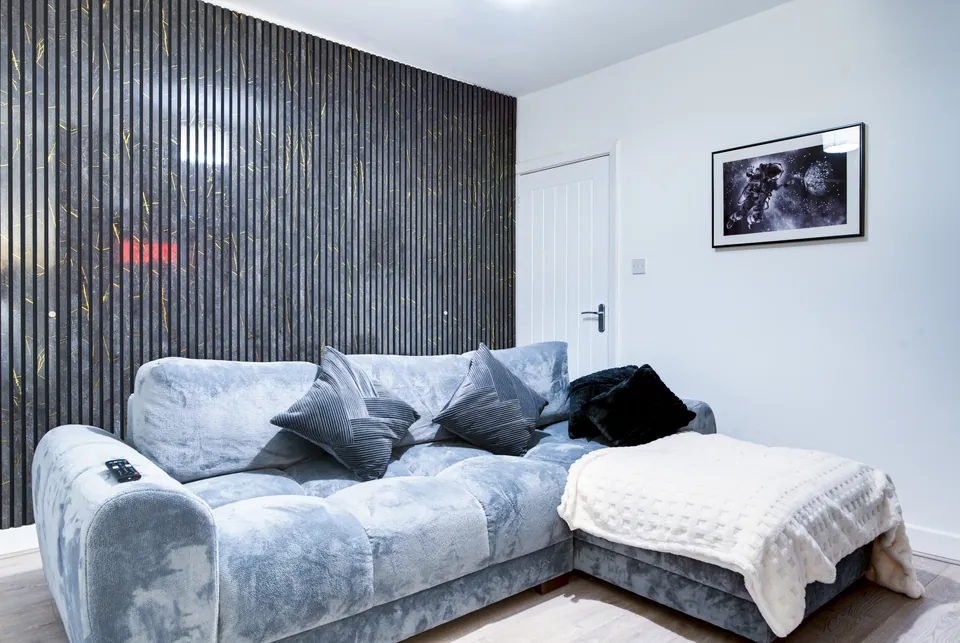 Grey velvet corner sofa against a dark slatted feature wall